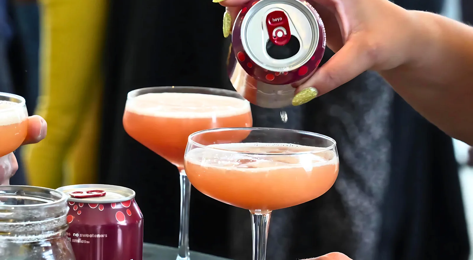 Two pink cocktails in coupe glasses being topped off at a mixology class